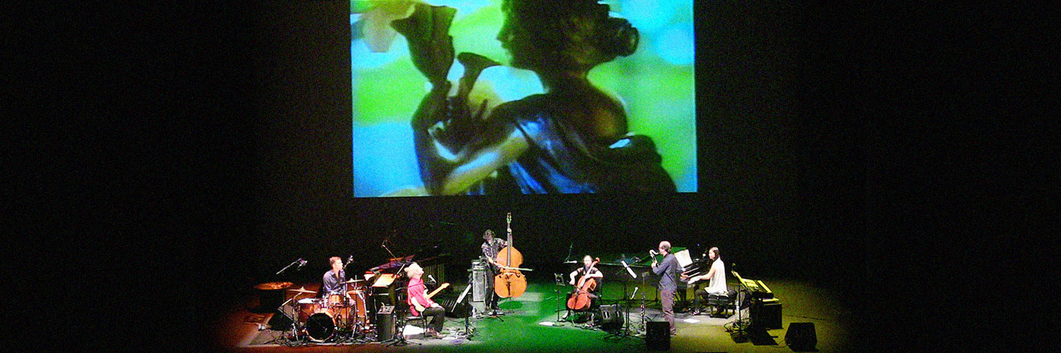The band on stage with a large digital projection of a woman in the background